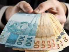 Mão segurando cédulas de R$ 100 e R$ 50