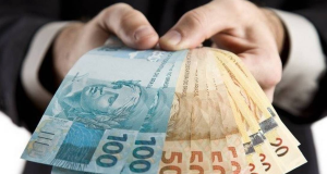 Mão segurando cédulas de R$ 100 e R$ 50