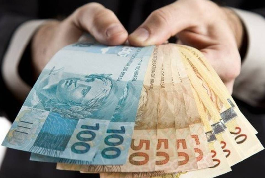 Mão segurando cédulas de R$ 100 e R$ 50