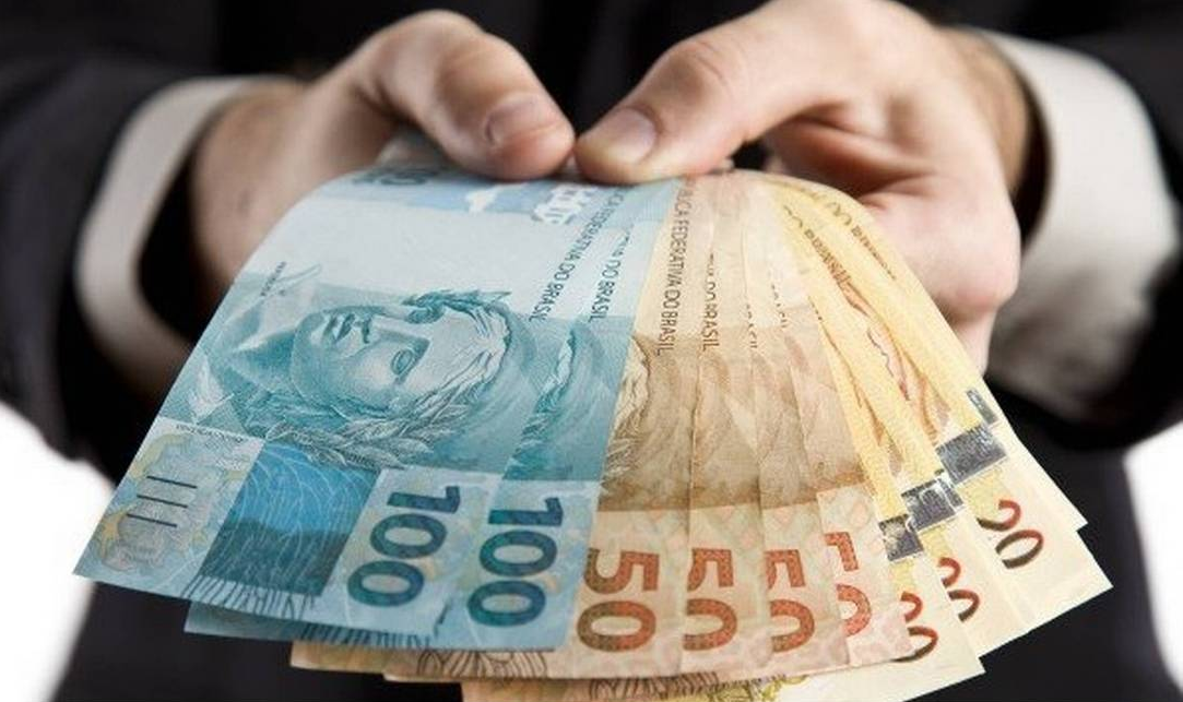 Mão segurando cédulas de R$ 100 e R$ 50