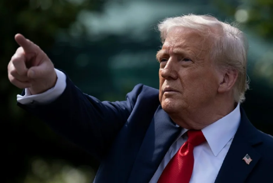 Donald Trump apontando pra frente, sério, de perfil