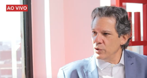 O ministro Fernando Haddad no canto direito de foto, falando, sério, olhando para o lado
