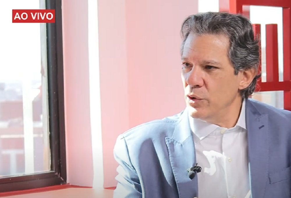 O ministro Fernando Haddad no canto direito de foto, falando, sério, olhando para o lado