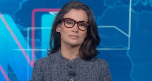 Renata Vasconcellos séria, olhando para a câmera, de óculos e roupa cinza