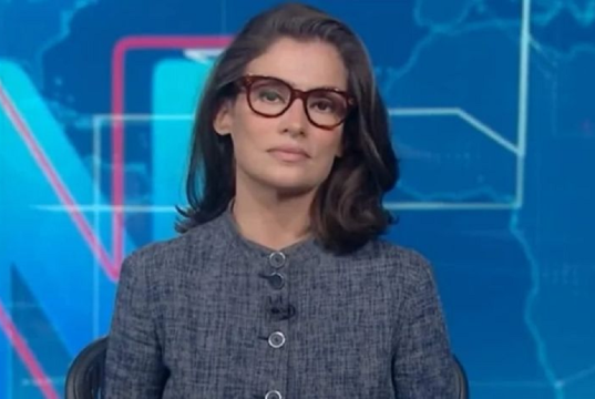Renata Vasconcellos séria, olhando para a câmera, de óculos e roupa cinza