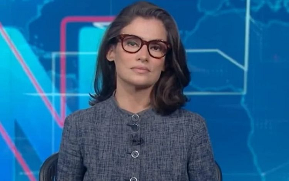 Renata Vasconcellos séria, olhando para a câmera, de óculos e roupa cinza