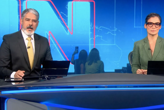 William Bonner e Renata Vasconcellos na bancada do Jornal Nacional, sérios, olhando para a câmera