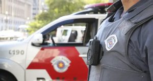 Agente da Polícia Militar de SP, sem mostrar o rosto, perto de carro