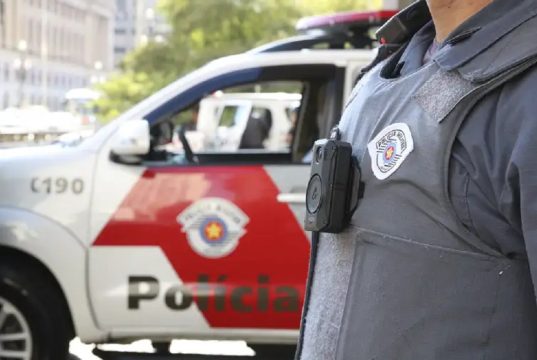 Agente da Polícia Militar de SP, sem mostrar o rosto, perto de carro