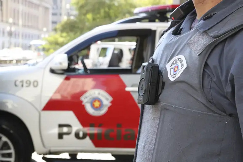 Agente da Polícia Militar de SP, sem mostrar o rosto, perto de carro