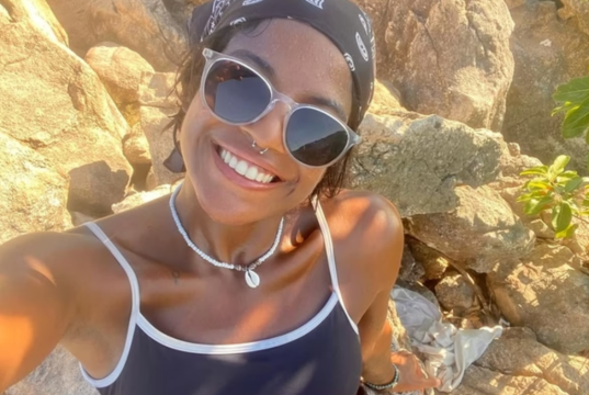 publicitária Juliana Marins de óculos escuros e bandana, olhando para a câmera, sorrindo