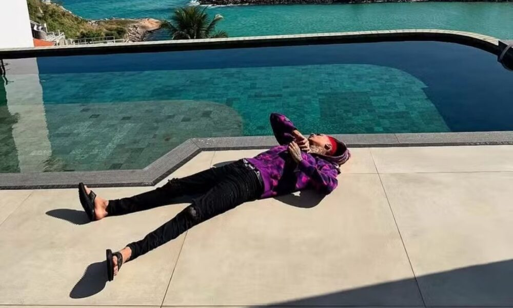 Oruam deitado à beira da piscina, vestindo roupa de frio