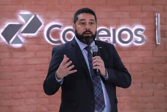 O presidente dos Correios, Fabiano Silva dos Santos, falando em microfone, sério