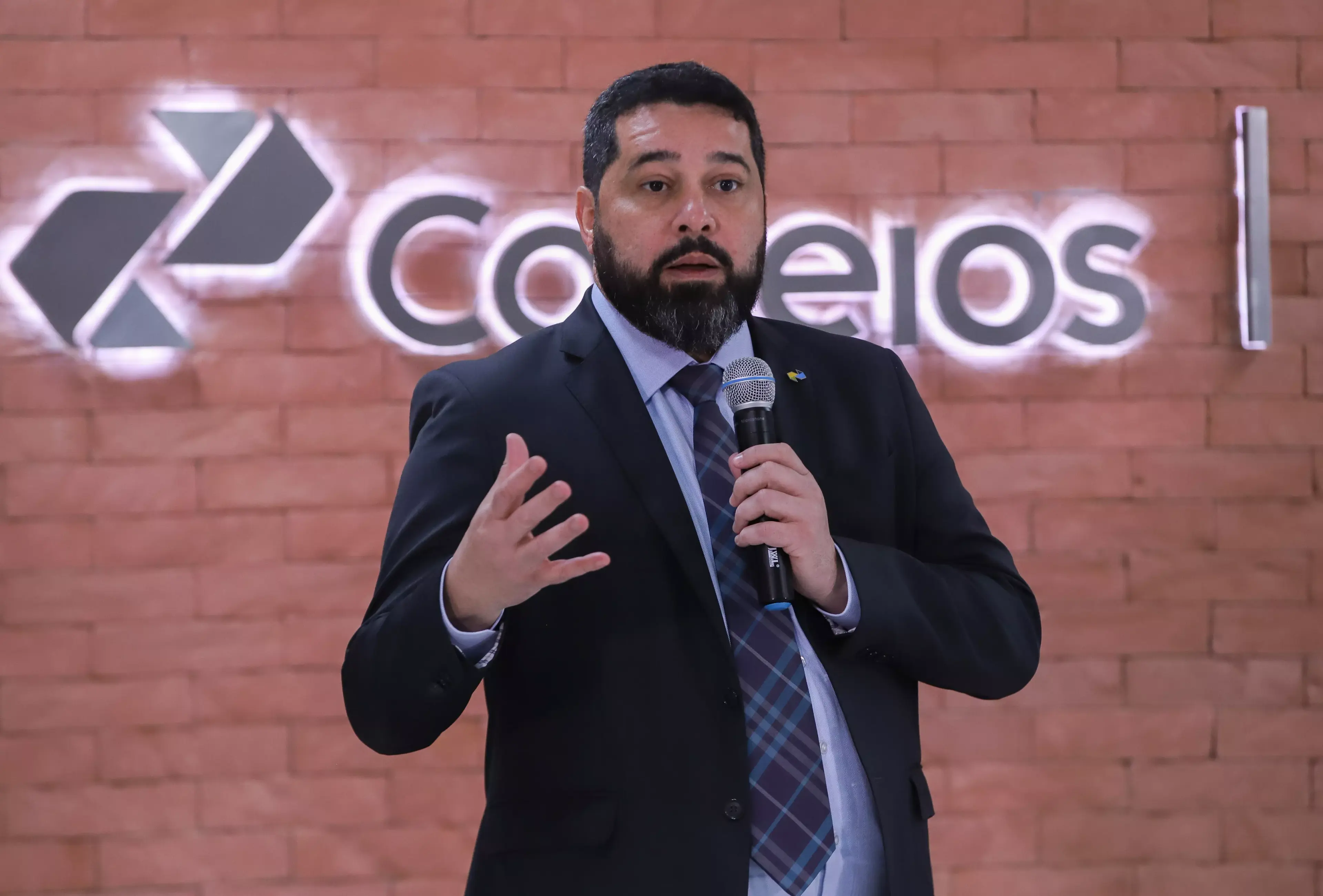 O presidente dos Correios, Fabiano Silva dos Santos, falando em microfone, sério