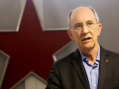 Rui Falcão falando, sério, com estrela vermelha ao fundo