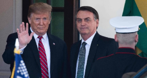 Donald Trump acenando e Jair Bolsonaro sério, ambos em pé, lado a lado