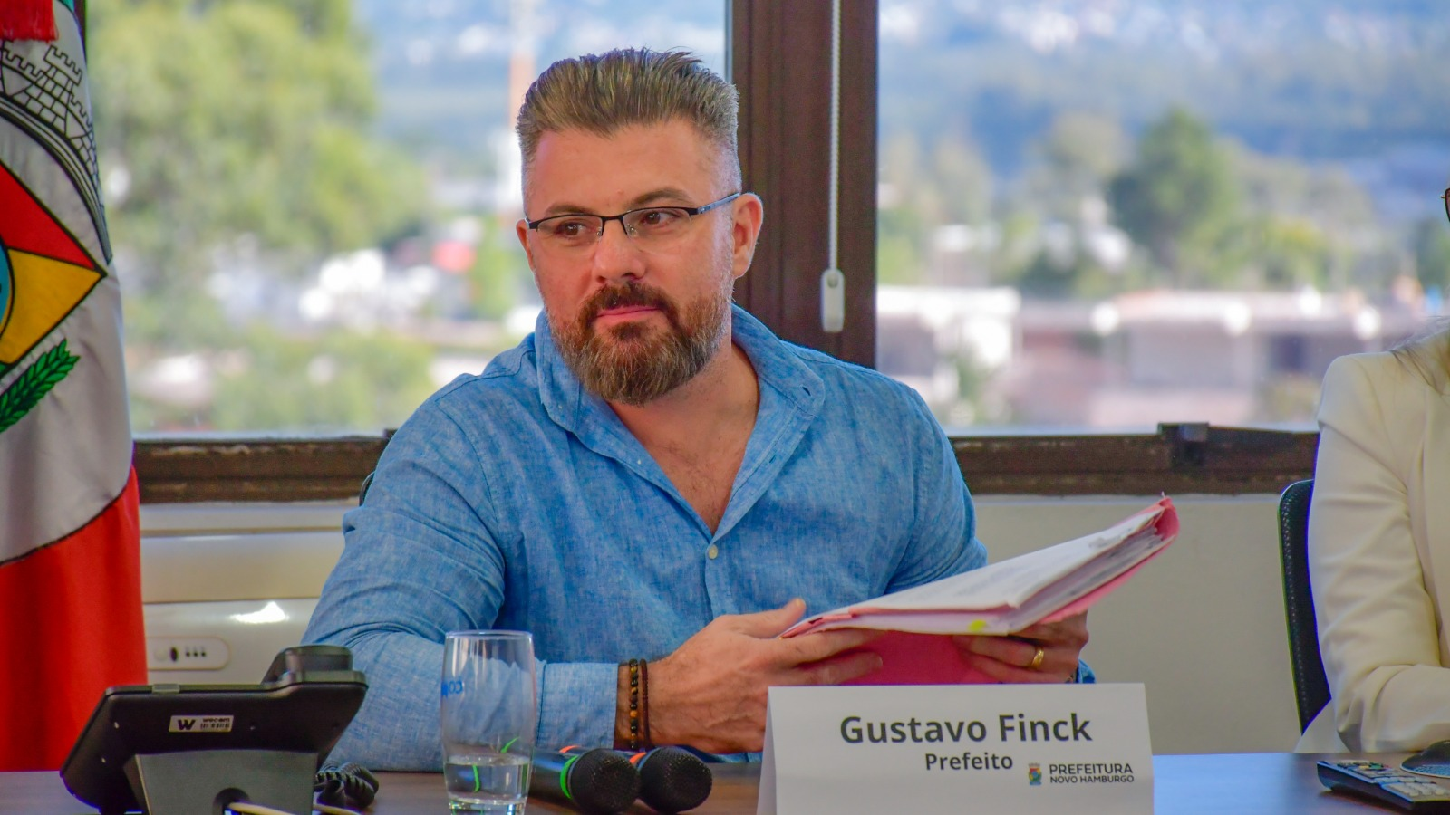prefeito Gustavo Finck (PP) de roupa social azul, de óculos, segurando papeis e olhando para o lado