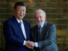 O presidente Xi Jinping e o presidente Lula sorrindo e olhando para a câmera durante aperto de mãos