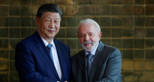 O presidente Xi Jinping e o presidente Lula sorrindo e olhando para a câmera durante aperto de mãos