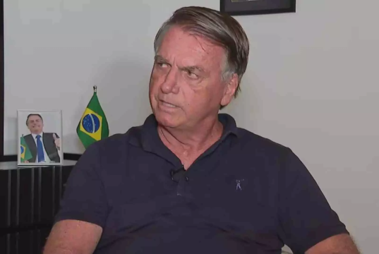 ex-presidente Jair Bolsonaro (PL) olhando para o lado, sério, de camisa azul marinho polo