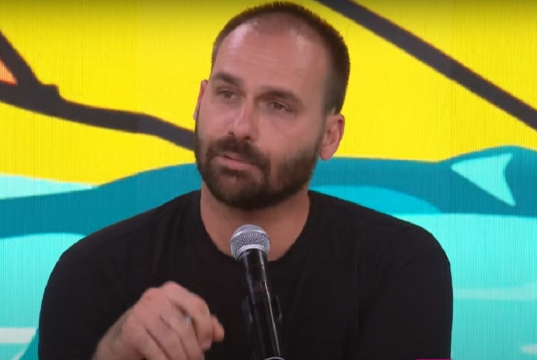 O deputado licenciado Eduardo Bolsonaro falando, sério, de roupa preta
