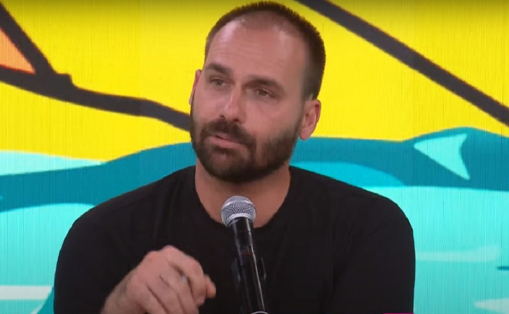 O deputado licenciado Eduardo Bolsonaro falando, sério, de roupa preta