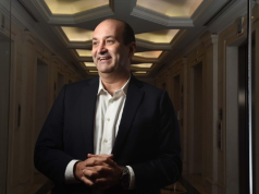 João Carlos Mansur, fundador da Reag, de roupa formal, sorrindo e olhando para o lado