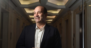 João Carlos Mansur, fundador da Reag, de roupa formal, sorrindo e olhando para o lado
