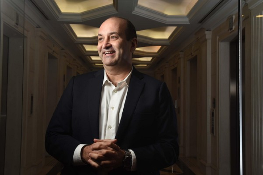 João Carlos Mansur, fundador da Reag, de roupa formal, sorrindo e olhando para o lado