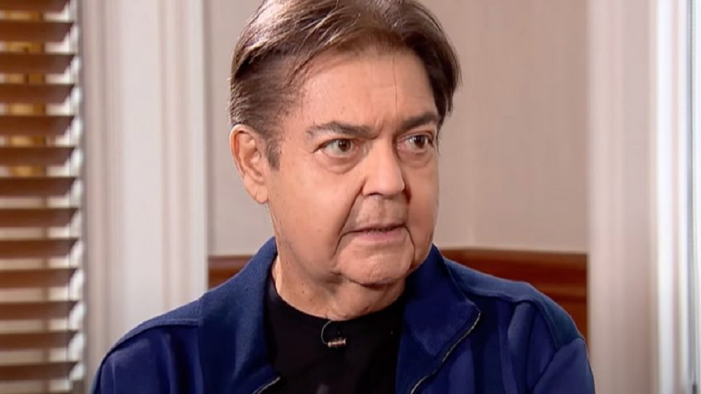 O apresentador Faustão olhando para o lado e falando, sério, de roupa de frio escura