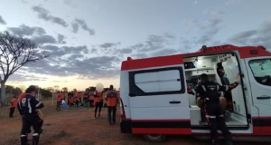 Ambulância em campo aberto com pessoas de roupas laranja em volta