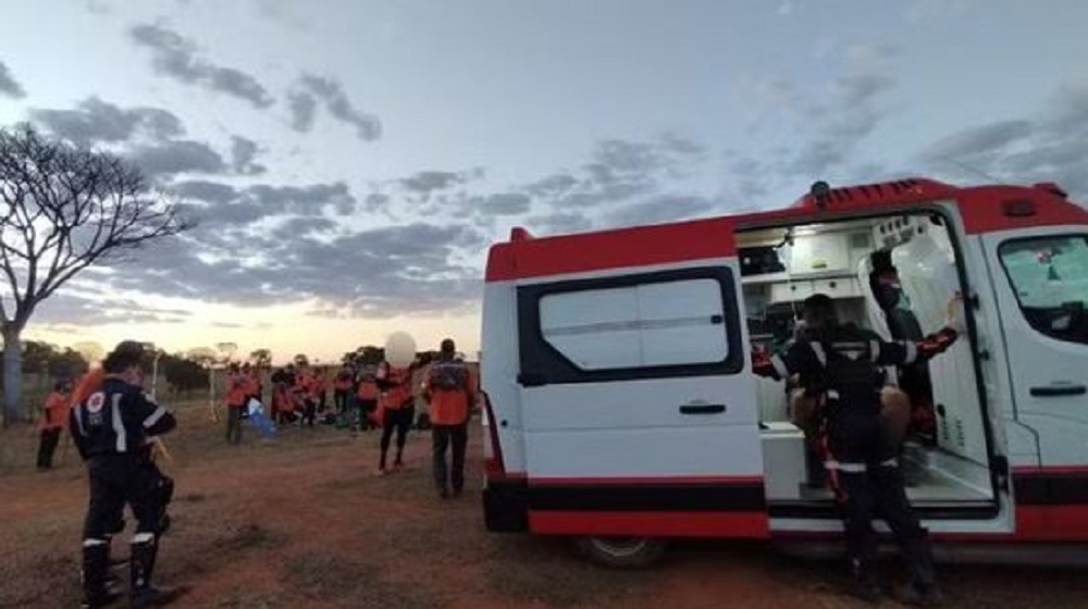 Ambulância em campo aberto com pessoas de roupas laranja em volta