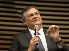 ministro Flávio Dino falando em microfone e gesticulando, de óculos