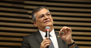ministro Flávio Dino falando em microfone e gesticulando, de óculos