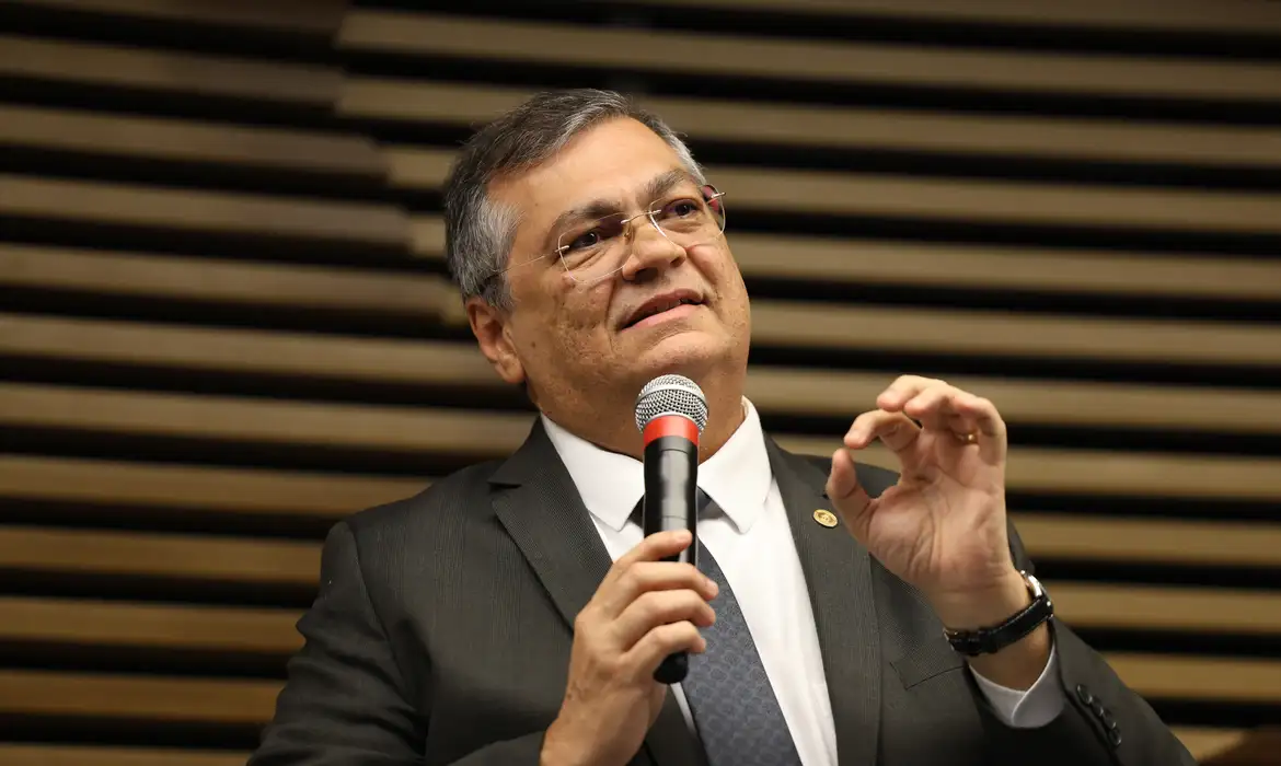 ministro Flávio Dino falando em microfone e gesticulando, de óculos