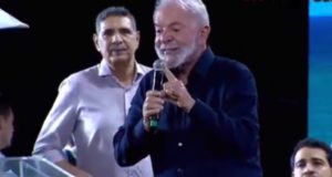 O presidente Lula (PT) de roupa social escura, falando em microfone e apontando, sério