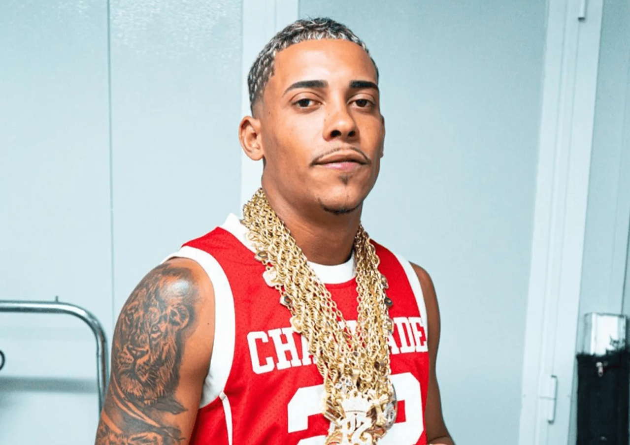 Marlon Brendon Coelho Couto da Silva, conhecido como MC Poze do Rodo, sério, de cordões de ouro e camiseta vermelha e branca, olhando para a câmera