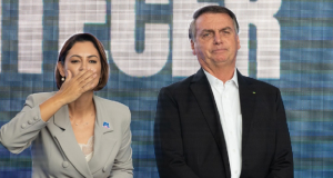 A ex-primeira-dama Michelle Bolsonaro (PL) e o ex-presidente Jair Bolsonaro (PL) lado a lado, em pé, ele sério e ela mandando beijo