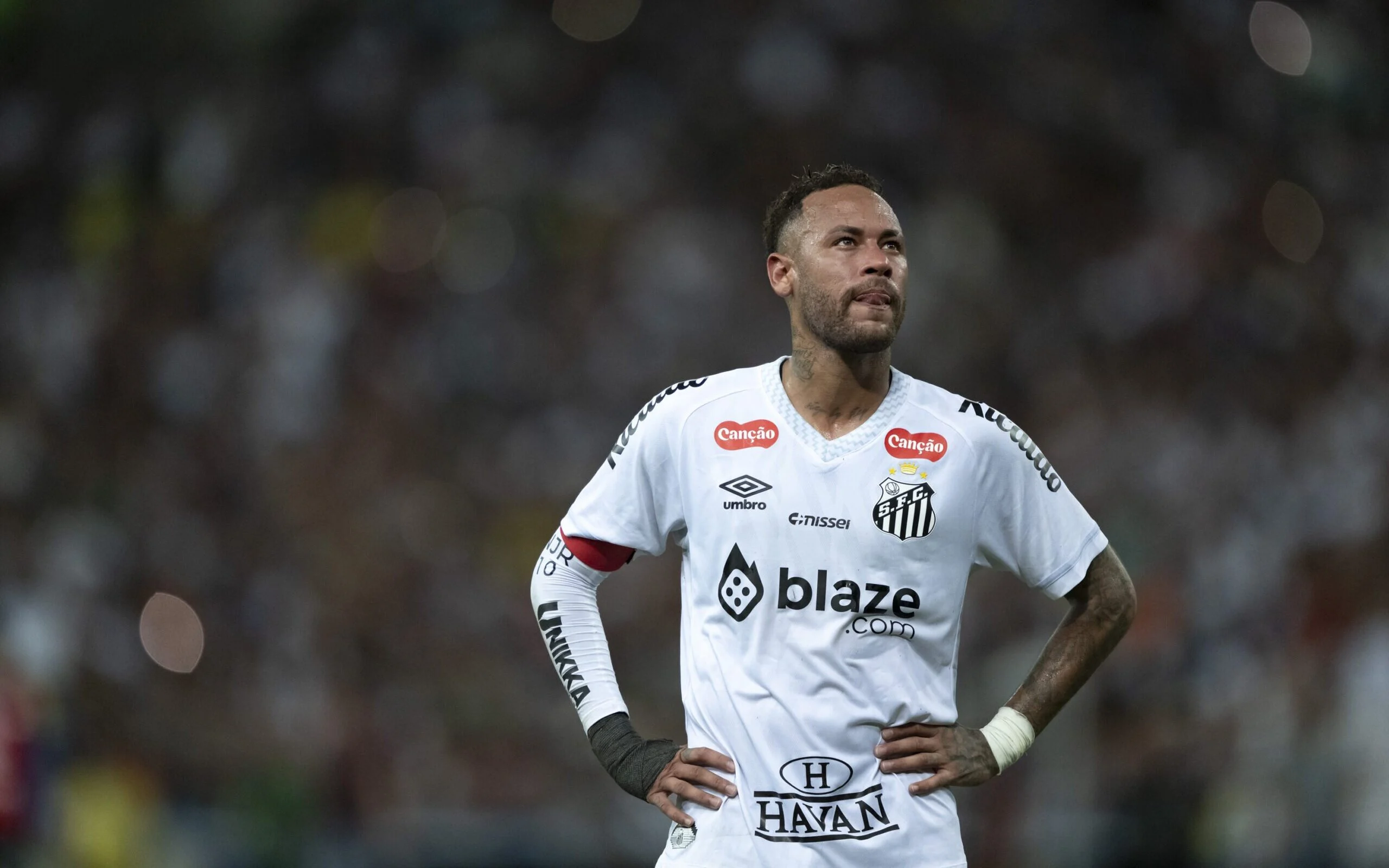 Neymar, jogador do Santos, olhando para o lado, com as mãos na cintura, sério, mostrando a língua