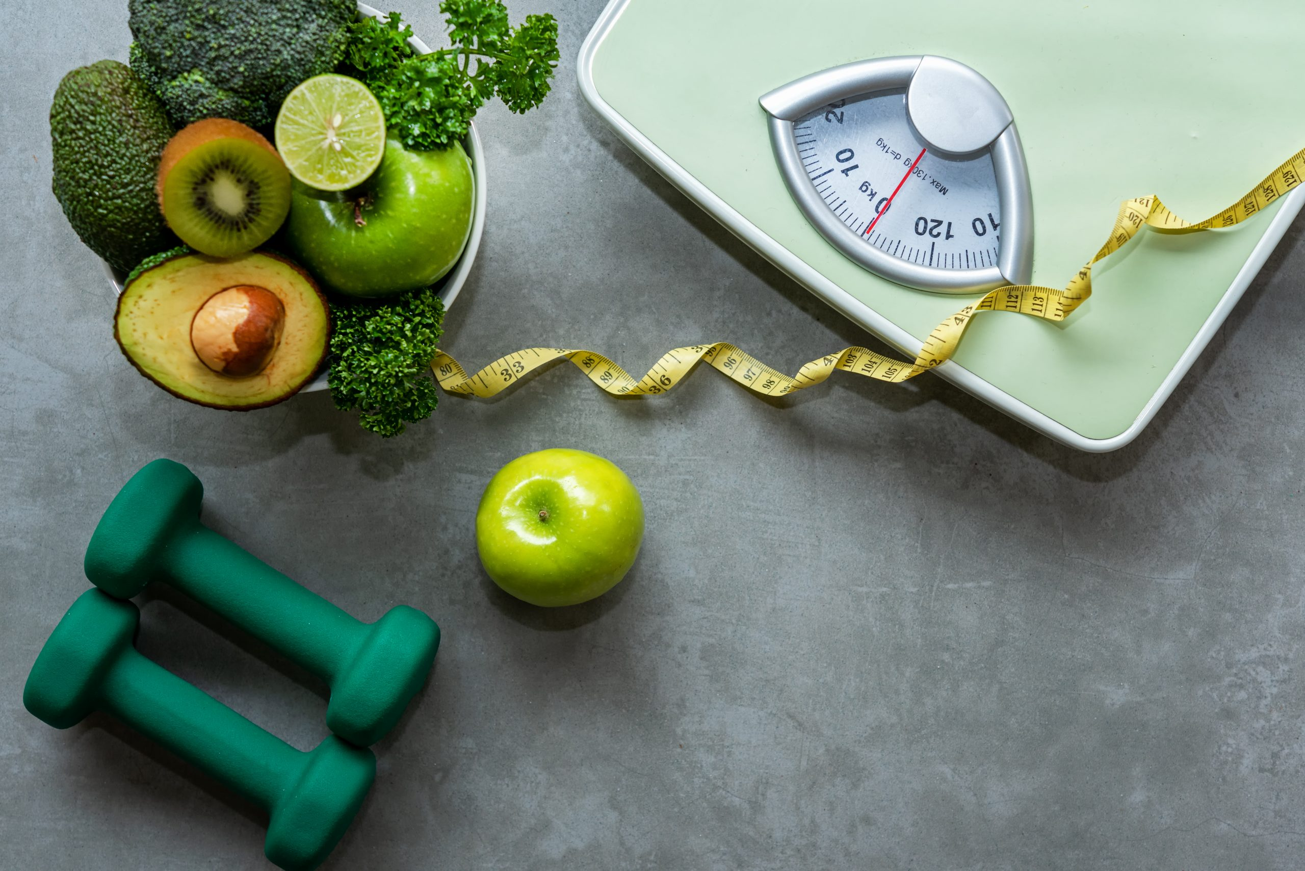 Imagem contendo fita métrica, verduras e legumes, pesos de academia e balança
