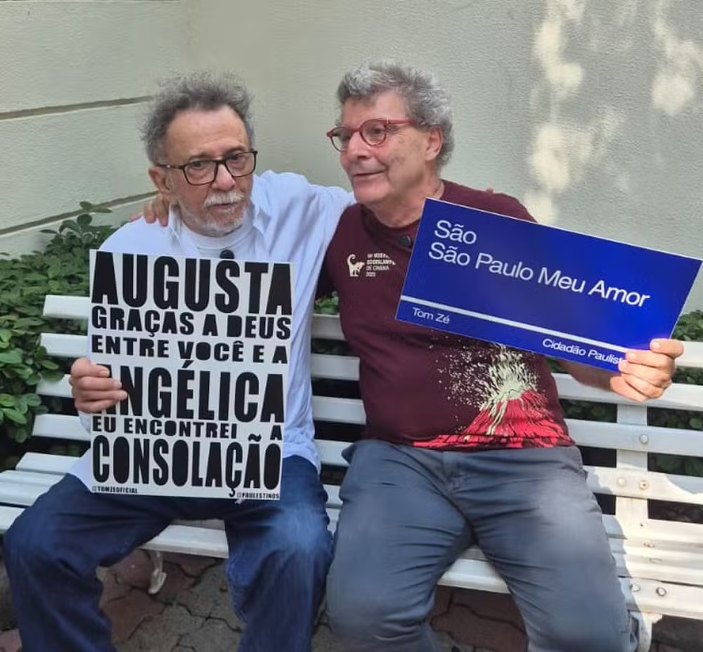O cantor Tom Zé e o vereador Nabil Bonduki (PT) sentados lado a lado com placas