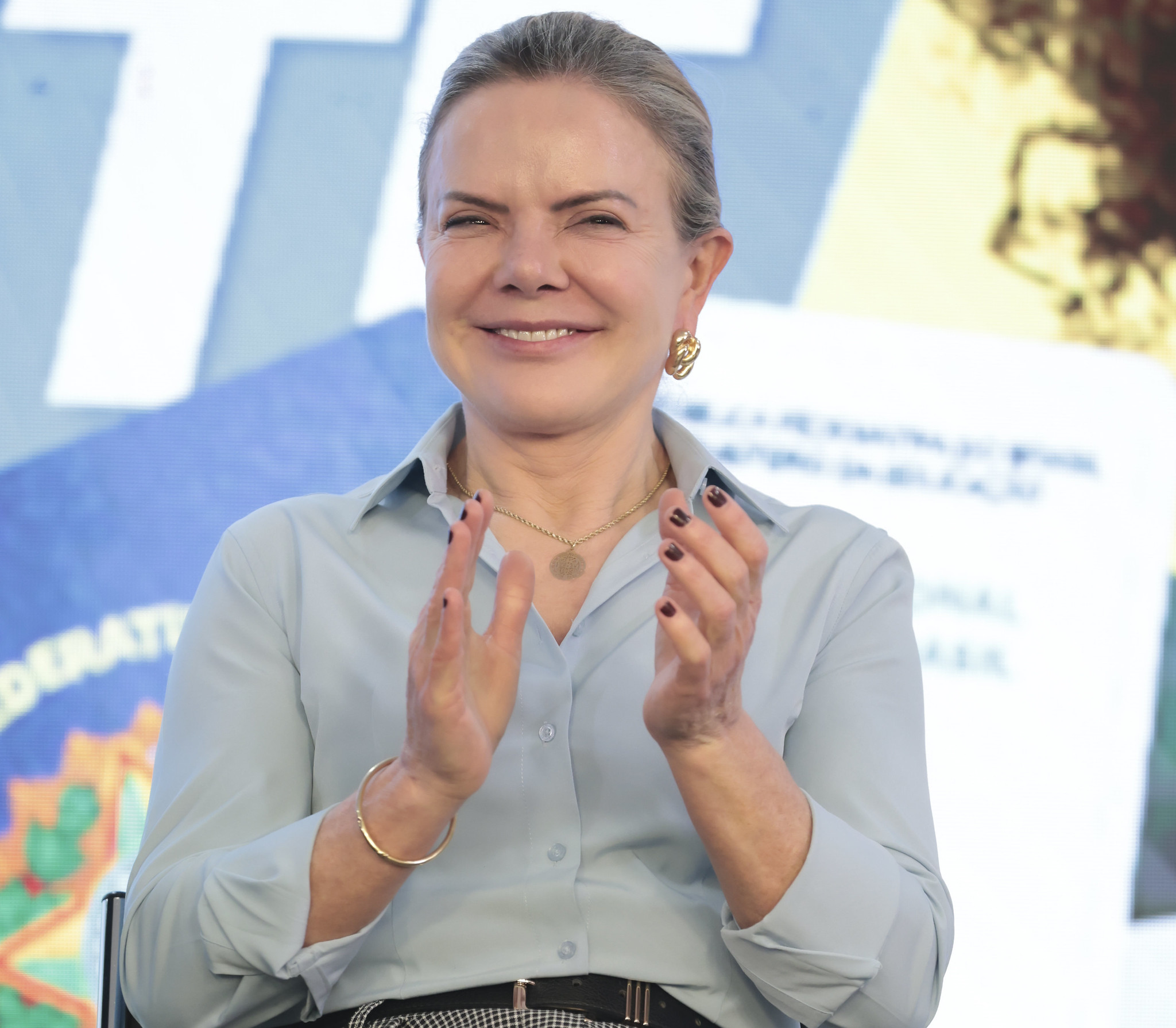 Gleisi Hoffmann, ministra de Relações Institucionais, de coque, com roupa social, sorrindo e batendo palmas
