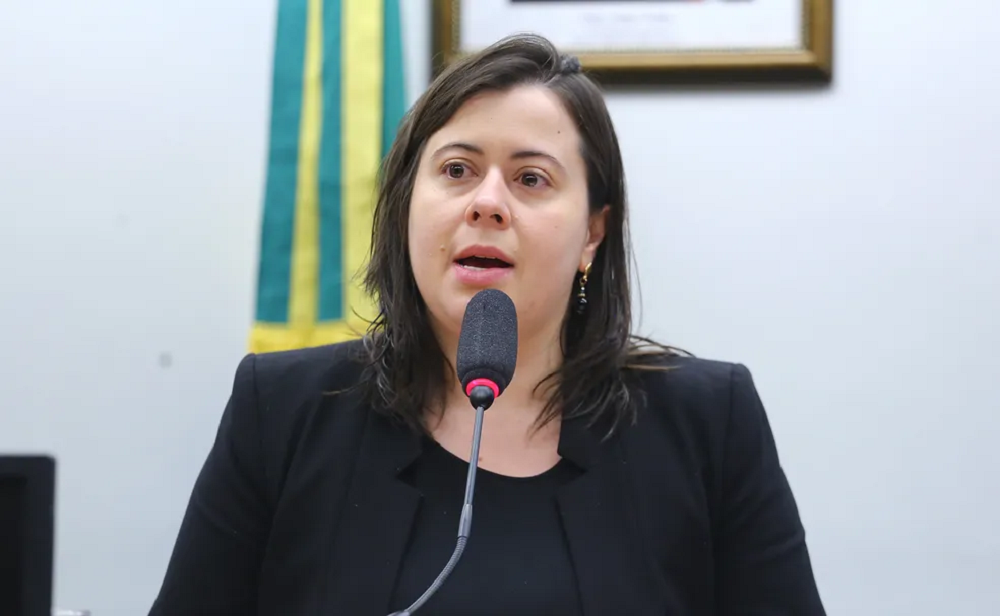 A deputada Sâmia Bomfim (PSOL-SP) de cabelo solto, séria, falando em microfone, de roupa preta, sem olhar para a câmera