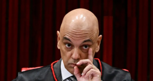 Alexandre de Moraes com expressão de alerta e mão próxima ao rosto, sério