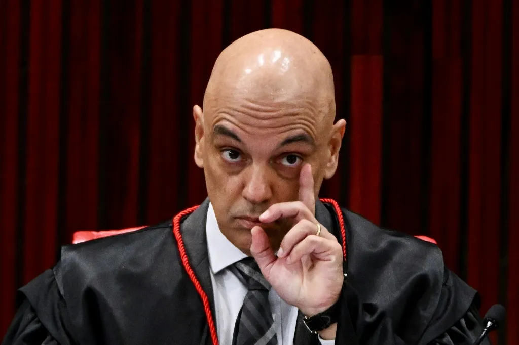 Alexandre de Moraes com expressão de alerta e mão próxima ao rosto, sério