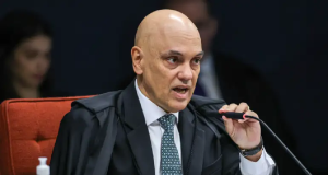 Alexandre de Moraes sério, segurando microfone e falando sem olhar para a câmera