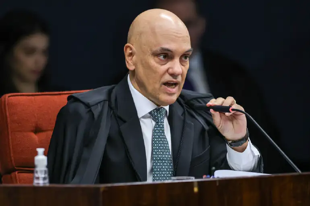 Alexandre de Moraes sério, segurando microfone e falando sem olhar para a câmera