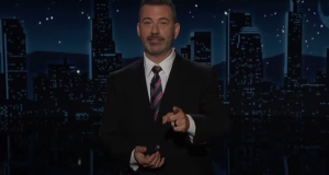 Jimmy Kimmel de roupa social, em pé, falando e apontando para a câmera