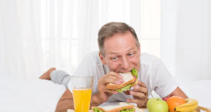 Homem tomando café da manhã deitado na cama de barriga para baixo