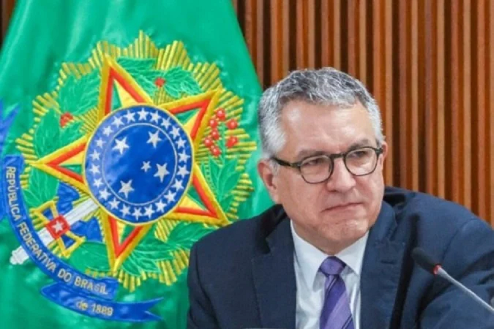 O ministro da Saúde, Alexandre Padilha, sério, olhando para o lado, de óculos, com bandeira ao fundo